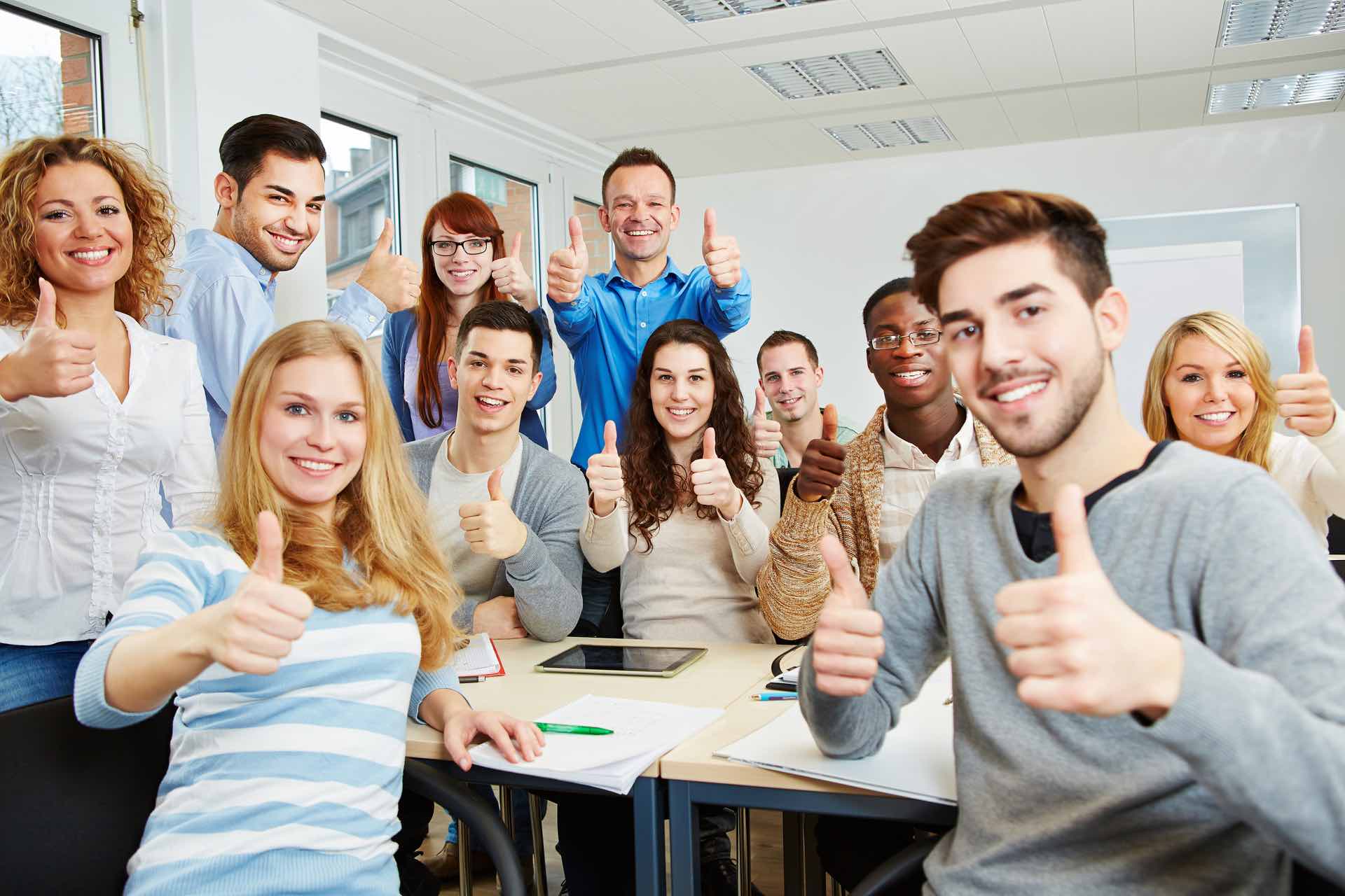 Many happy students with teacher holding their thumbs up in university